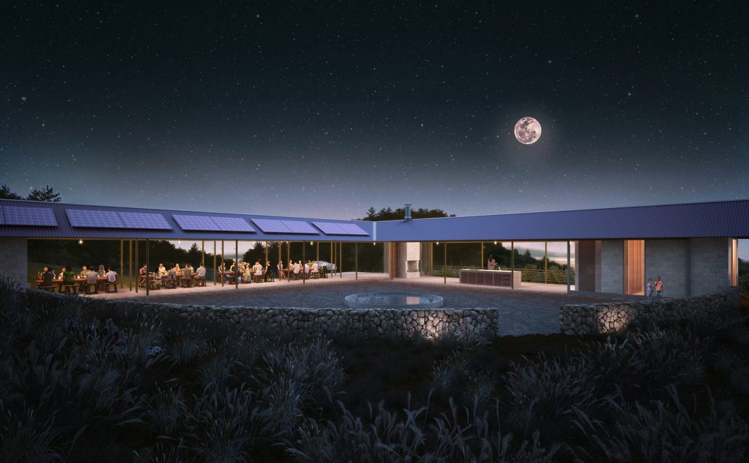 Night view of a courtyard with a stone-ringed plunge pool, long dinner tables under an open solar-roofed structure, and a full moon above